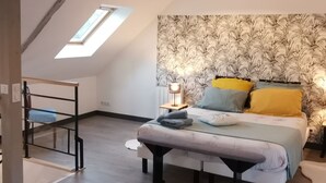 Une chambre avec un plafond en pente, un puits de lumière, un lit avec une literie à motifs, un banc et une table en bois.