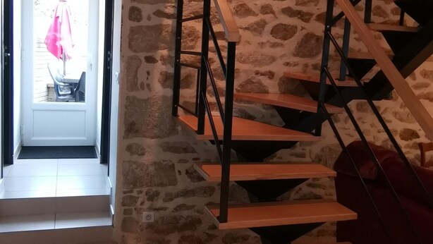 Un escalier avec des marches en bois et des rampes en métal, adossé à un mur de pierre.