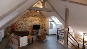 Une pièce mansardée chaleureuse avec des murs en pierre, une télévision, un canapé et une petite table.