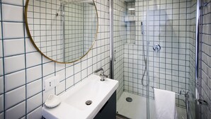 Kylpyhuone, jossa on valkoinen pesuallas, pyöreä peili ja lasiseinällä varustettu suihku.