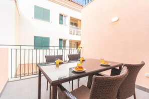 A balcony with a table set for breakfast, wicker chairs, and a view of a building with balconies. - Cassia Loft by Atlantic Holiday (Funchal)