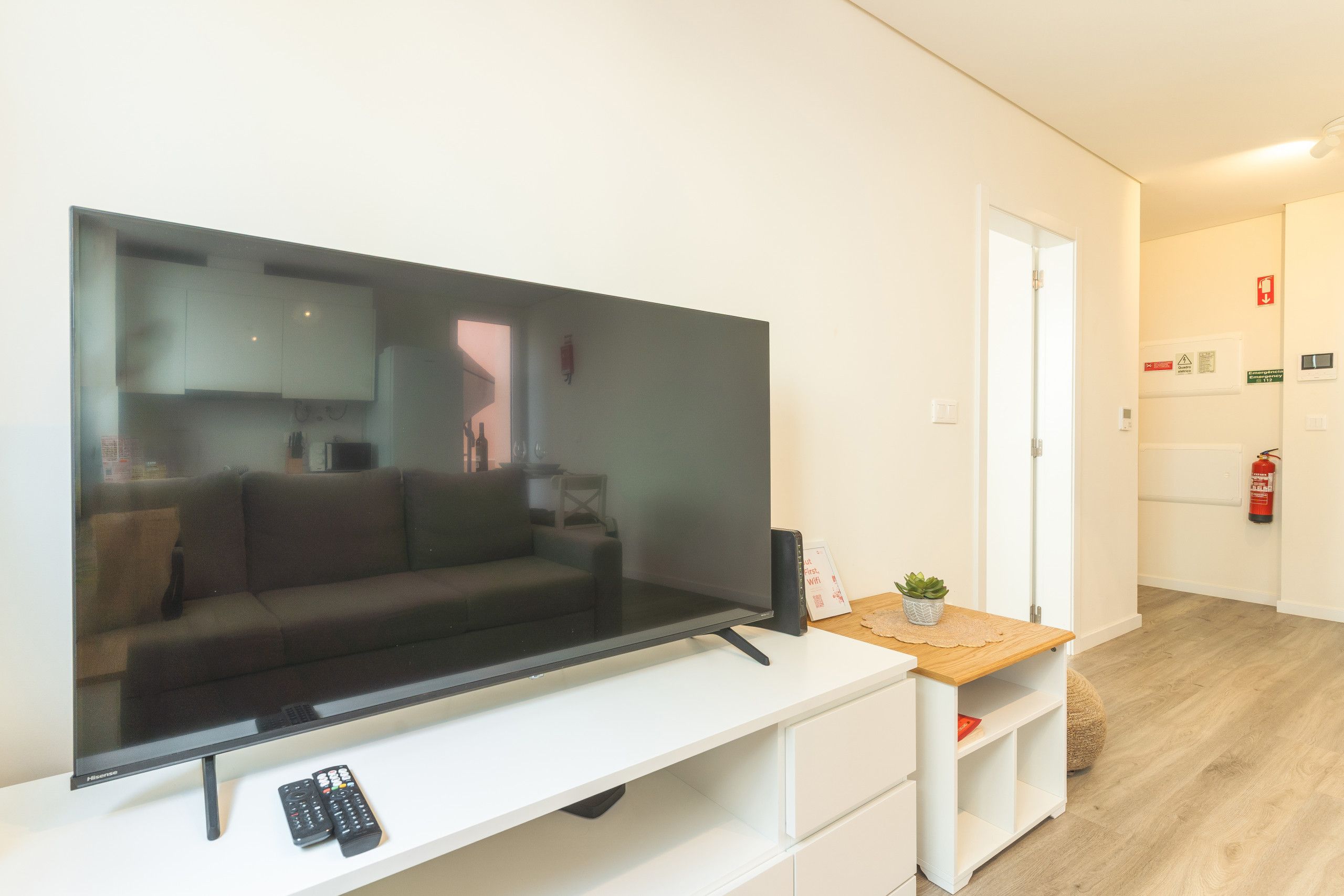 Un salon moderne avec un grand téléviseur à écran plat posé sur un meuble blanc, un canapé et une petite table sur laquelle se trouve une plante.