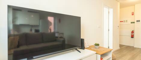 A modern living room with a large flat-screen TV on a white entertainment unit, a sofa, and a small table with a plant.