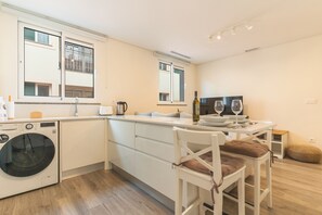 A modern kitchen with a built-in washing machine, a dining area with a table set for two, and a large window providing natural light.