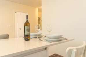 A dining area with a table set for two, featuring a bottle of wine, two wine glasses, and white plates. - Cassia Loft by Atlantic Holiday (Funchal)