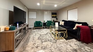 A living room with a TV, green chairs, a black sofa, and a patterned rug.