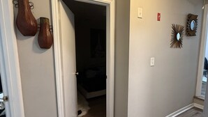 A hallway with wooden flooring, a door leading to a bedroom, and decorative wall art.