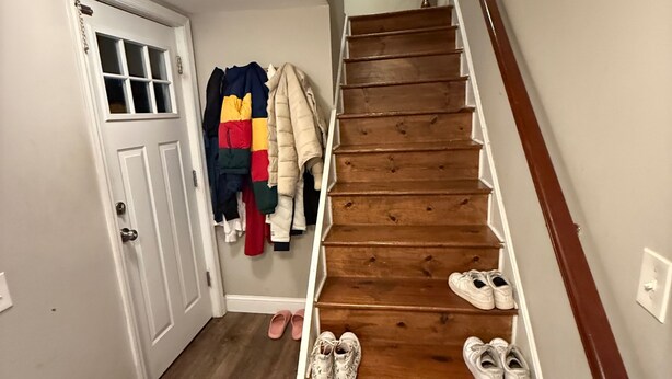 A staircase with wooden steps and a white handrail, leading to a landing with a white door and a window.