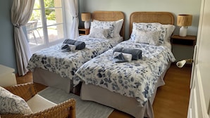 A room with two beds, each with a floral-patterned bedspread, a wicker chair, and a small table with a lamp. - Beautiful gite set among vineyards with hot tub and use of heated swimming pool (Loubens)