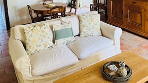 A cozy living room with a white sofa, wooden dining table, and a kitchen area with a refrigerator and stove. - Beautiful gite set among vineyards with hot tub and use of heated swimming pool (Loubens)