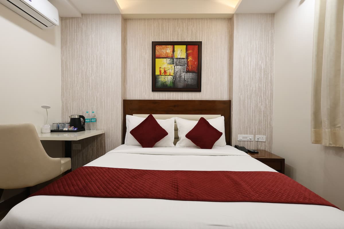 A hotel room with a bed, a desk, a chair, a coffee maker, and a painting on the wall.