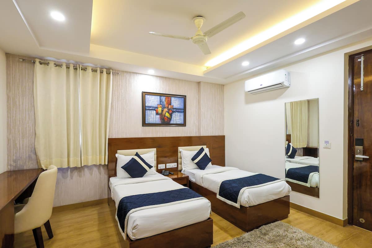A hotel room with two single beds, a desk, a chair, a ceiling fan, an air conditioning unit, and a large mirror.