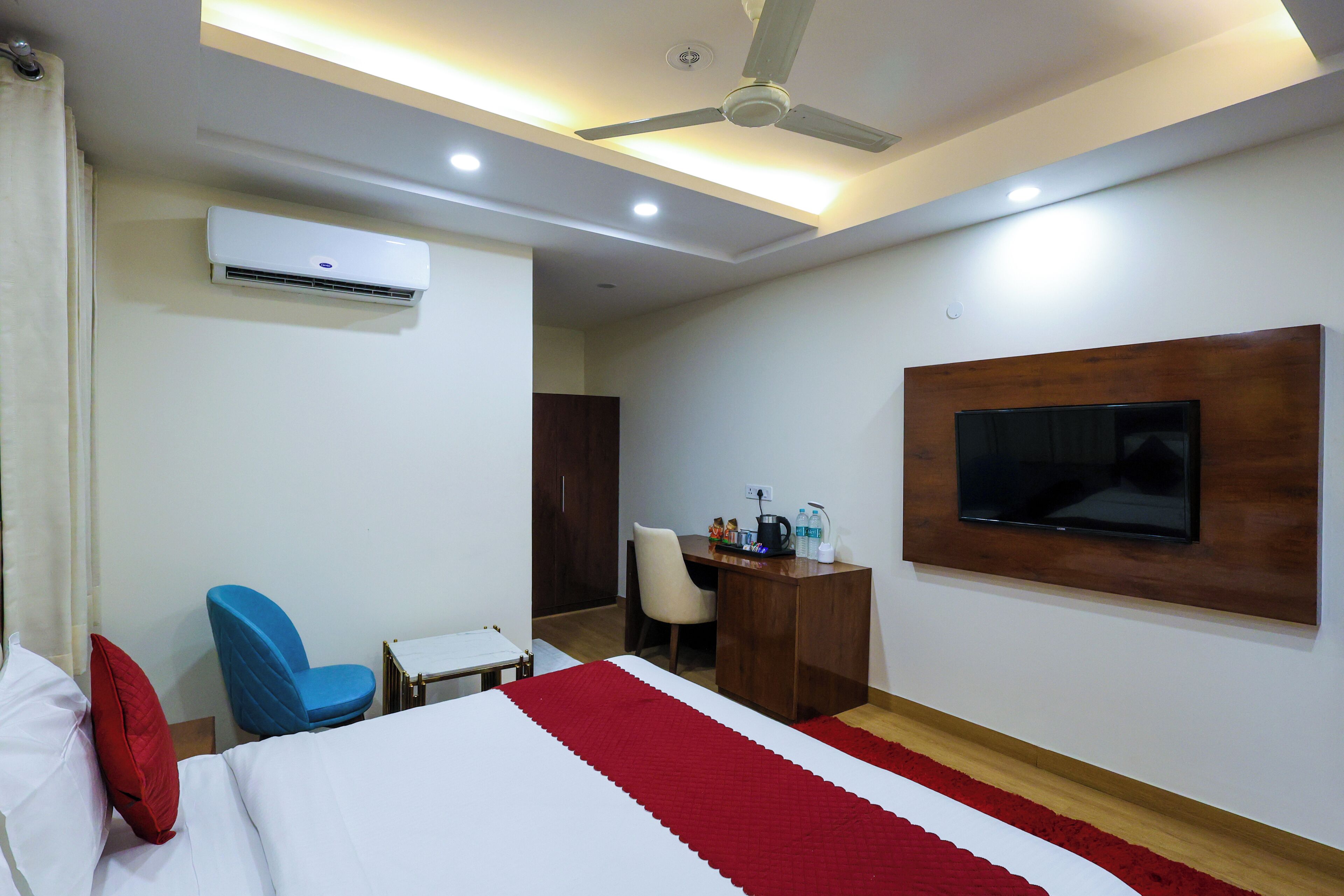 A hotel room with a bed, a desk, a chair, a television, and an air conditioning unit.