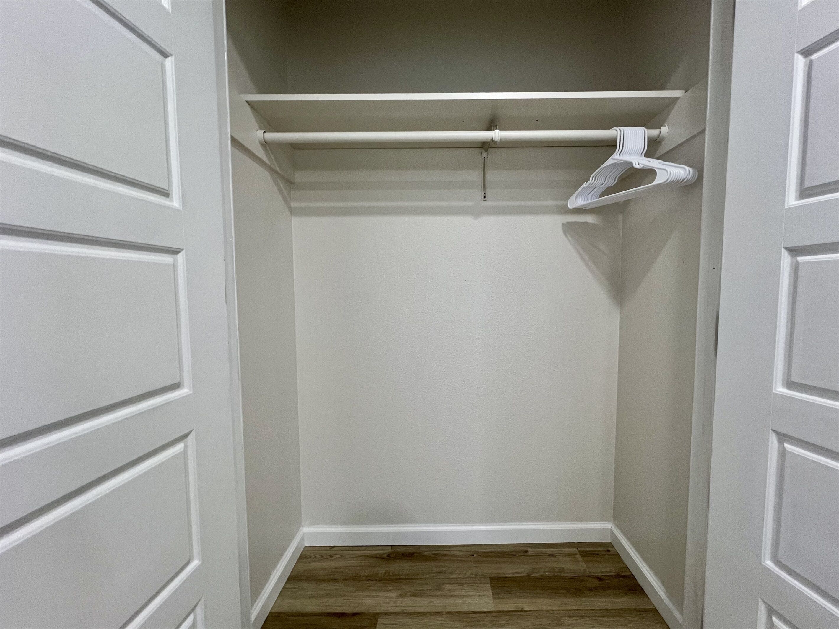 Un vestidor con paredes blancas, piso de madera y una barra para colgar blanca.