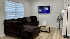 Una sala moderna con un sofá seccional marrón oscuro, una pequeña mesa de centro de madera, un televisor de pantalla plana montado en la pared y una planta en maceta.