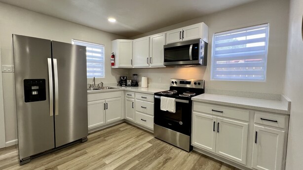 Una cocina moderna con electrodomésticos de acero inoxidable, armarios blancos y piso de madera.