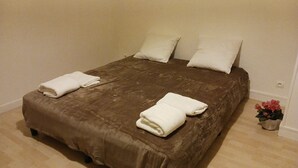 A neatly made bed with a brown bedspread and two pillows, a small potted plant with pink flowers, and a white wall. - 2 rooms 37M2 4p.tout neuf.limite Paris12e.30mn DISNEY, 9mn CHAMPS ELYSEE+LOUVRE  (Vincennes)