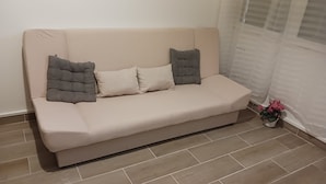 A beige sofa with three cushions in a room with tiled flooring and a potted plant. - 2 rooms 37M2 4p.tout neuf.limite Paris12e.30mn DISNEY, 9mn CHAMPS ELYSEE+LOUVRE  (Vincennes)