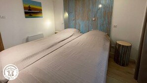 A double bed with a striped headboard, a small round table, and a painting on the wall. - Modern house with AC, garden and parking, near Noirmoutier beach (Barbâtre)
