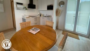 A modern kitchen with white cabinets, a wooden dining table, and a large window. - Modern house with AC, garden and parking, near Noirmoutier beach (Barbâtre)