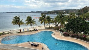 Una piscina de diseño curvo, rodeada de palmeras y vistas a la playa.