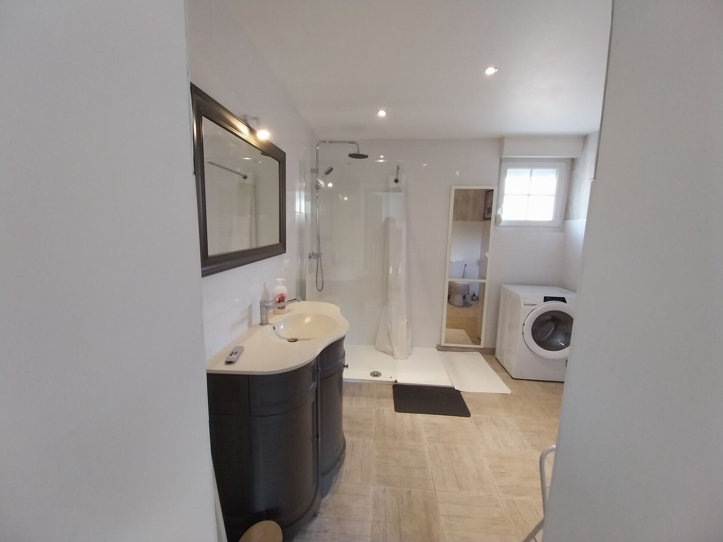 Un baño moderno con lavamanos, espejo, ducha y lavadora.