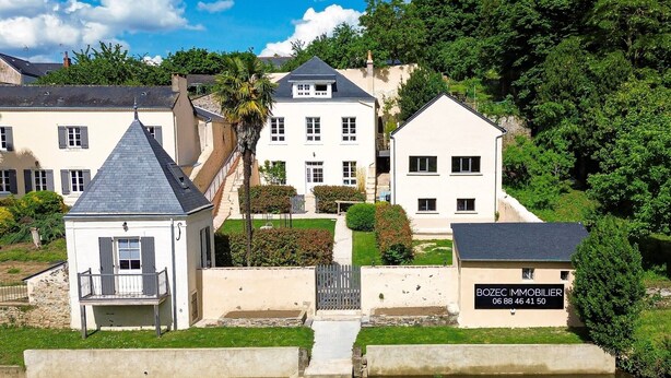 Ett bostadsområde med en vattenyta i förgrunden, en vit byggnad med skylten ”BOZEC IMMOBILIER” i bakgrunden och ett stort hus med ett grått tak.