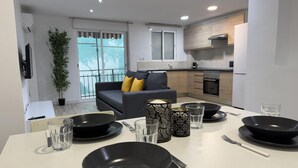 Una cocina moderna con comedor, un sofá gris con cojines amarillos y un ventanal con vistas a un balcón.