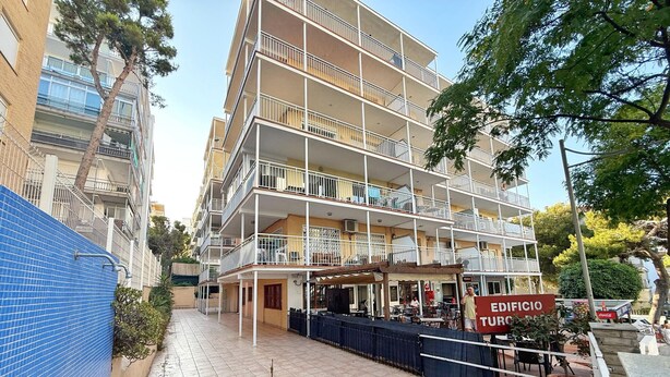 Un edificio de varios pisos con balcones, una terraza con asientos al aire libre y un escaparate visible.