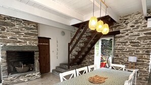 A dining area with a stone fireplace, a staircase, and a table with chairs. - Spacious house with garden in the heart of Lomener (Groix)
