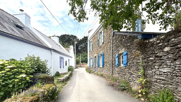 A narrow road flanked by stone and white buildings with blue shutters. - Spacious house with garden in the heart of Lomener (Groix)