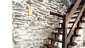 A stone wall with a wooden spiral staircase and a yellow sign. - Spacious house with garden in the heart of Lomener (Groix)