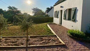 A white building with a sloped roof and green shutters, surrounded by a garden with a small tree and gravel paths. - Charming house near beach in Groix, 2 bedrooms (Groix)