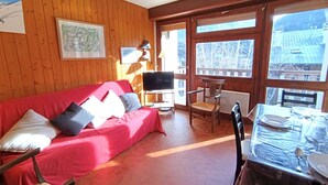 Um quarto acolhedor com um sofá vermelho, paredes de madeira, uma televisão e uma mesa de jantar com capa protetora.