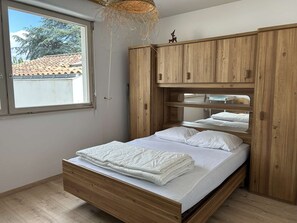Une pièce avec un lit, une armoire en bois et une fenêtre.