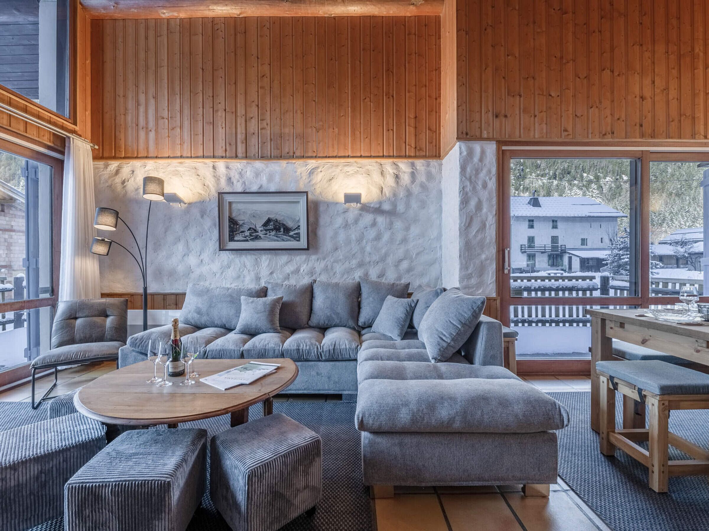 Una sala de estar acogedora con un sofá gris, una mesa de centro de madera y un ventanal con vistas a un paisaje nevado.