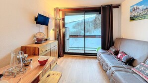 Een gezellige woonkamer met een houten salontafel, een bank en een aan de muur bevestigde televisie.