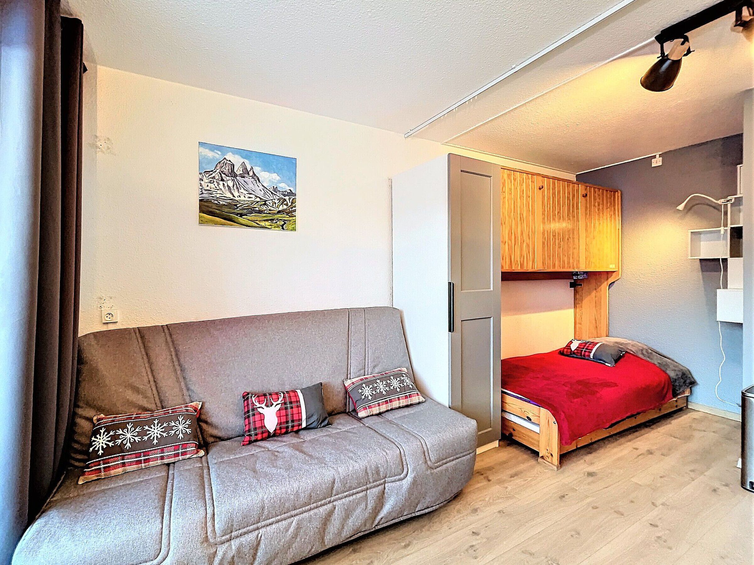 Une pièce chaleureuse avec un canapé gris, un lit rouge et une armoire en bois.