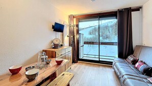 Een gezellige woonkamer met een houten tafel, een bank en een groot raam met uitzicht op een besneeerd landschap.