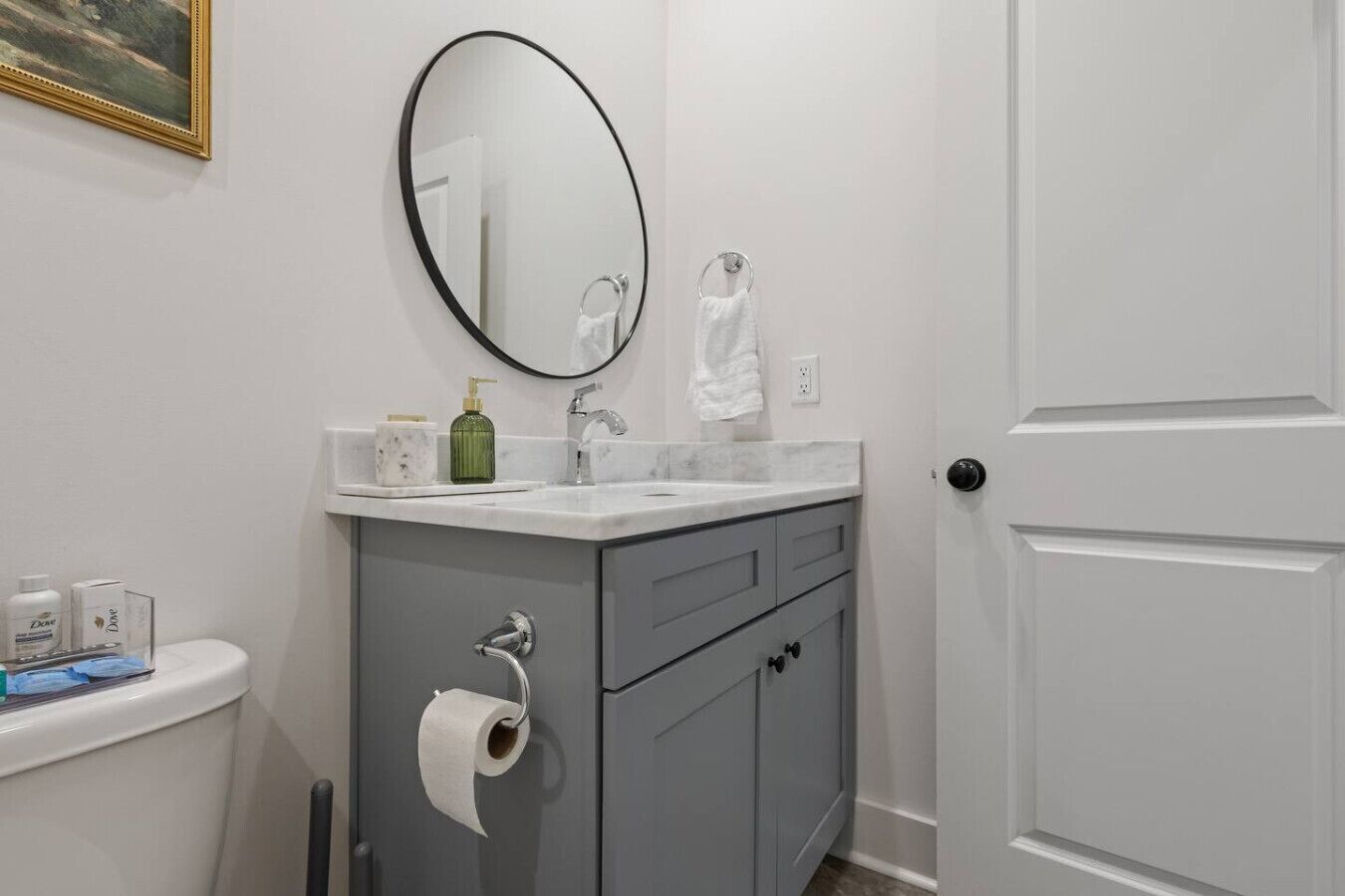 A bathroom with a white toilet, a grey cabinet with a mirror above the sink, and a white door.