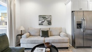 Ein modernes Wohnzimmer mit einem beigefarbenen Sofa, einem Couchtisch, einem Gemälde an der Wand und einem Edelstahl-Kühlschrank.