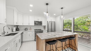 Una cocina moderna con armarios blancos, electrodomésticos de acero inoxidable, una isla de mármol y taburetes negros.