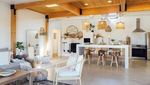 Un espacio habitable amplio con techo de madera, un comedor con taburetes de bar, una cocina con electrodomésticos modernos y una chimenea.