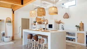 Cocina moderna con isla central, taburetes de bar, lámparas de mimbre colgantes y un backsplash de ladrillo blanco.