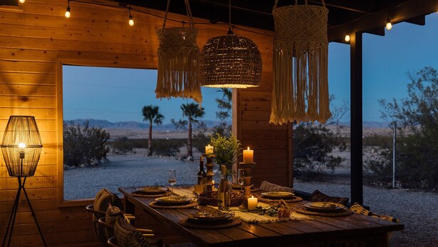 Un comedor de madera con una mesa dispuesta para cuatro personas, velas y lámparas colgantes de macramé.
