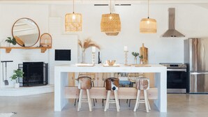 Una cocina moderna con una isla central, luces colgantes, una estufa integrada y un espejo grande sobre la isla.