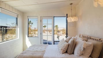 Ein Schlafzimmer mit Bett, Kissen, einem Nachttisch und Blick auf eine Wüstenlandschaft durch eine Schiebetür.