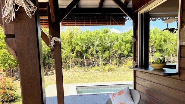 Eine Außenpatio mit einer Holzhütte, eine gepolsterte Sitzgruppe mit einem kleinen Tisch und Blick auf einen Garten und Pool.