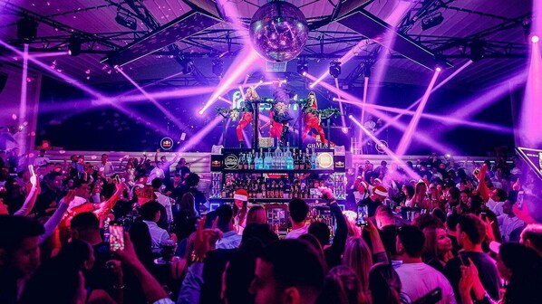 A crowded indoor event with a stage, bar area, and audience.
