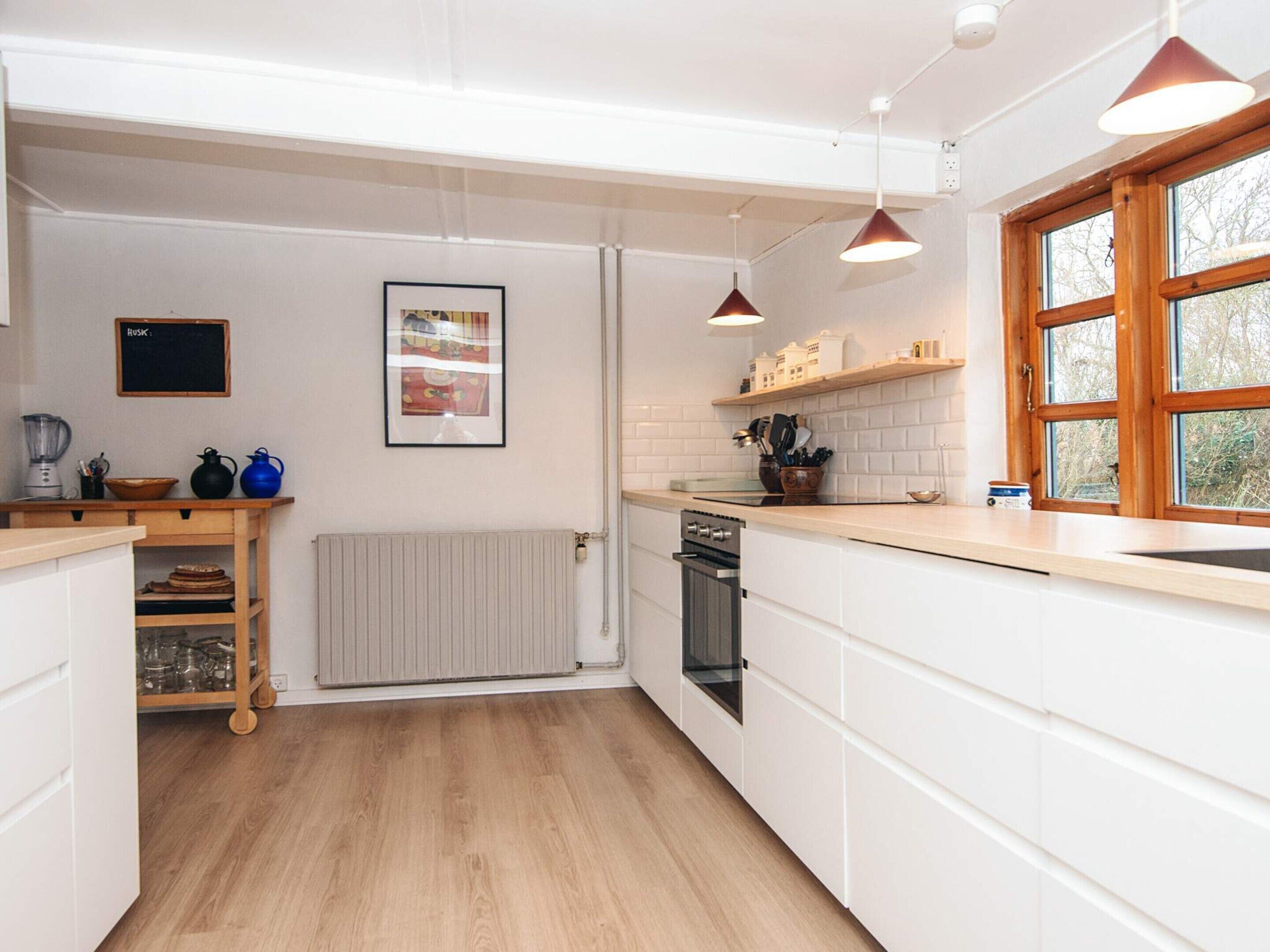 A modern kitchen with white cabinetry, a wooden countertop, a built-in oven, and pendant lighting.